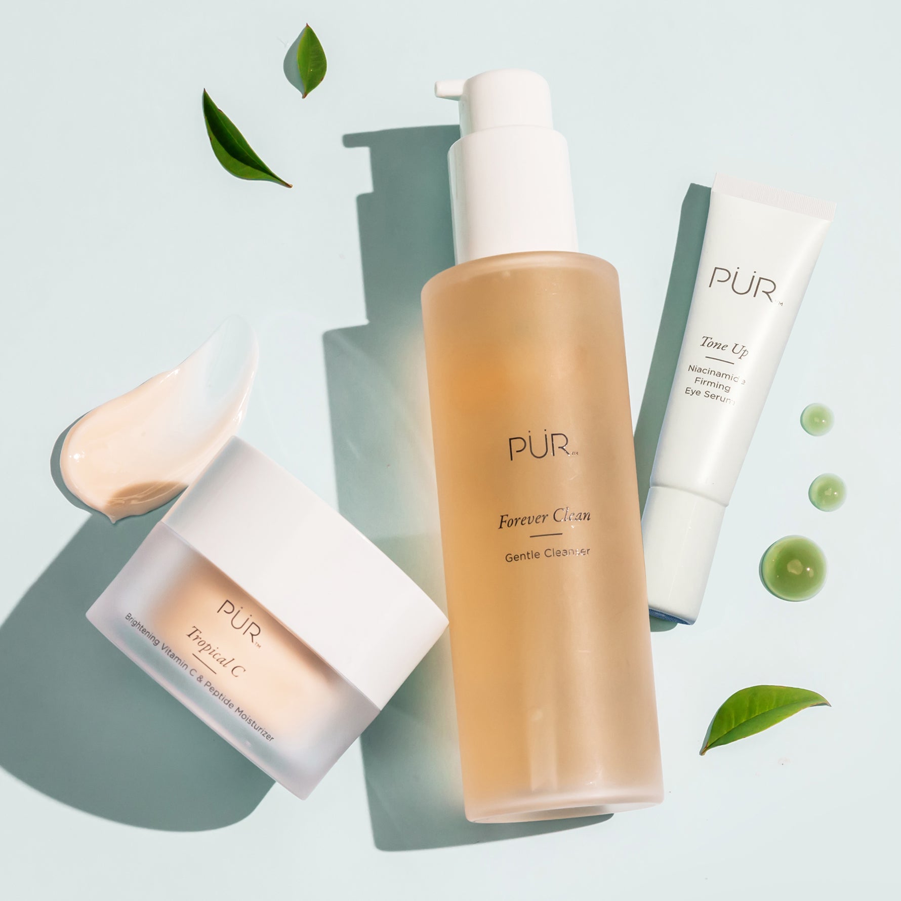 PÜR Tropical C Moisturizer displayed with PÜR Forever Clean Gentle Cleanser and Tone Up Eye Serum on pastel background, surrounded by green leaves and product textures.